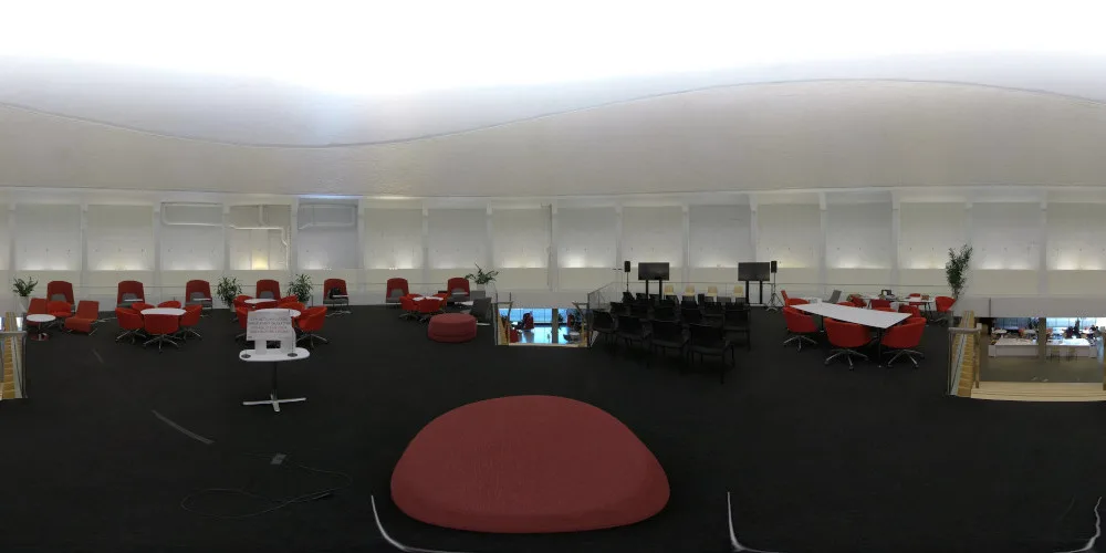 Vue à 360° de l’étage du dôme : plafond blanc, fauteuils et tables rouges en périphérie, et un grand pouf rouge rond au centre